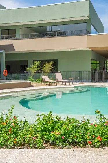 Piscina, jardim florido e lounge ao fundo